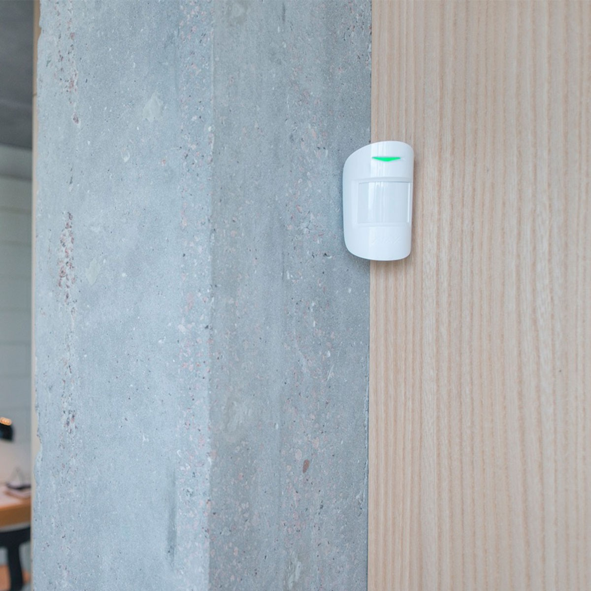 Sensor de seguridad blanco montado en madera clara y pared de hormigón.