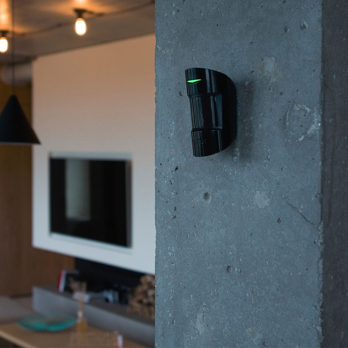 Un sensore di sicurezza, nero e montato su un muro grigio, con una luce verde.