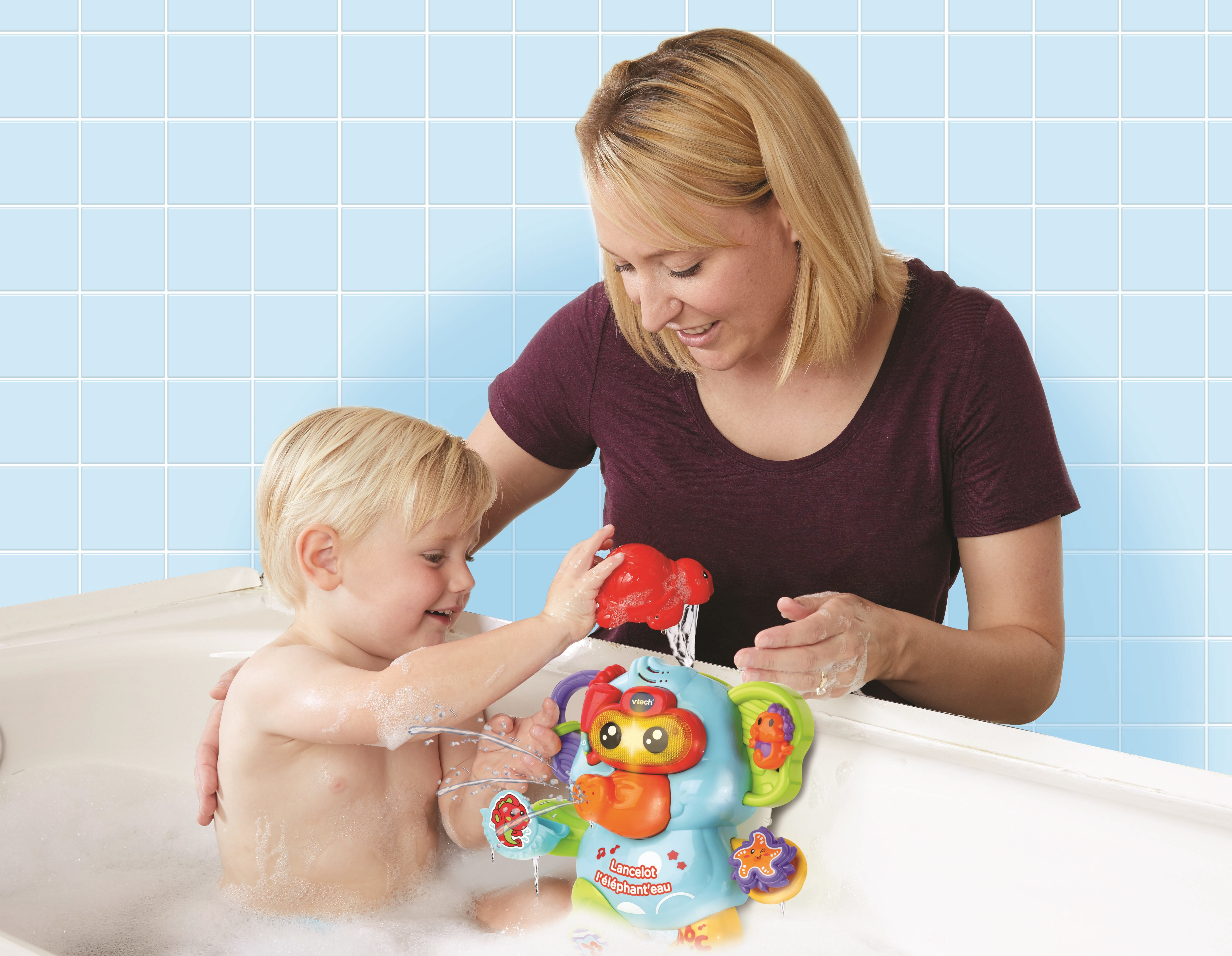 Małe dziecko i matka bawią się niebieską zabawką do kąpieli w kształcie słonia w wannie, rozpylając wodę.