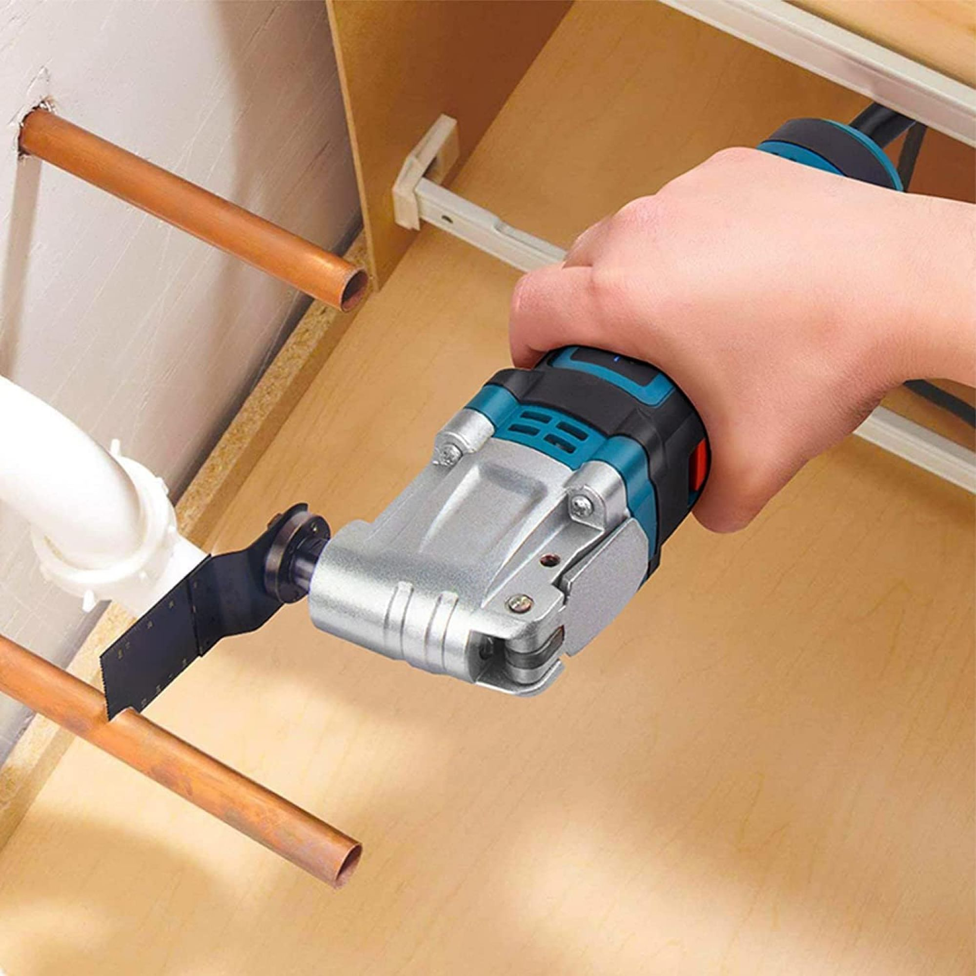 Eine Hand, die ein Elektrowerkzeug hält und Kupferrohre in einem Holzschrank schneidet. Sägeblatt ist sichtbar.