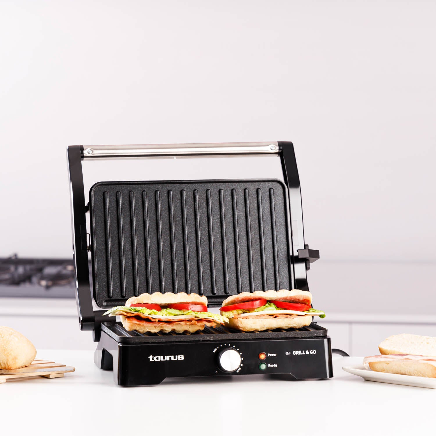 Schwarzer Grill mit zwei Sandwiches. Die Sandwiches haben Fleisch, Tomaten und Salat. Weißer Hintergrund.