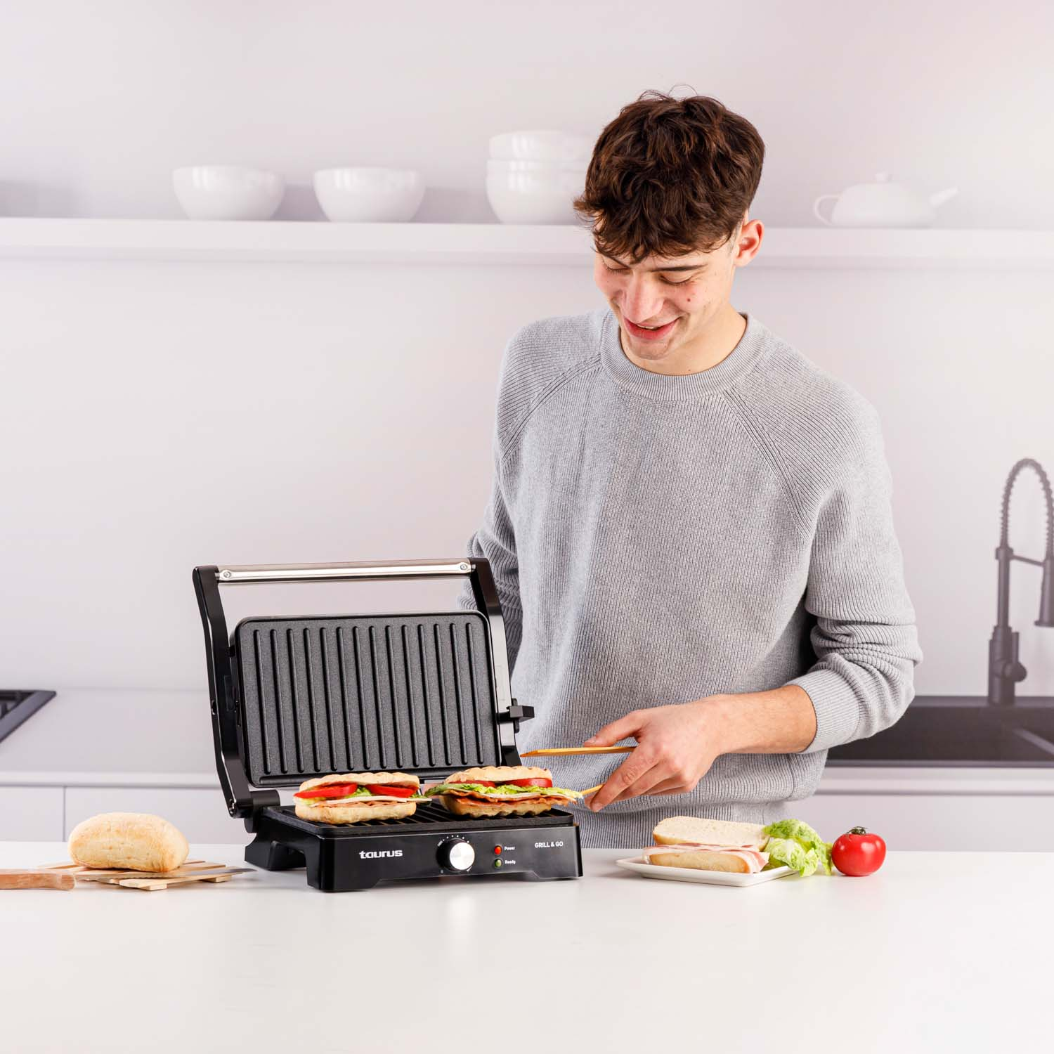 Ein Mann grillt Sandwiches. Er hält einen Holzspatel. Der Grill hat zwei Sandwiches.