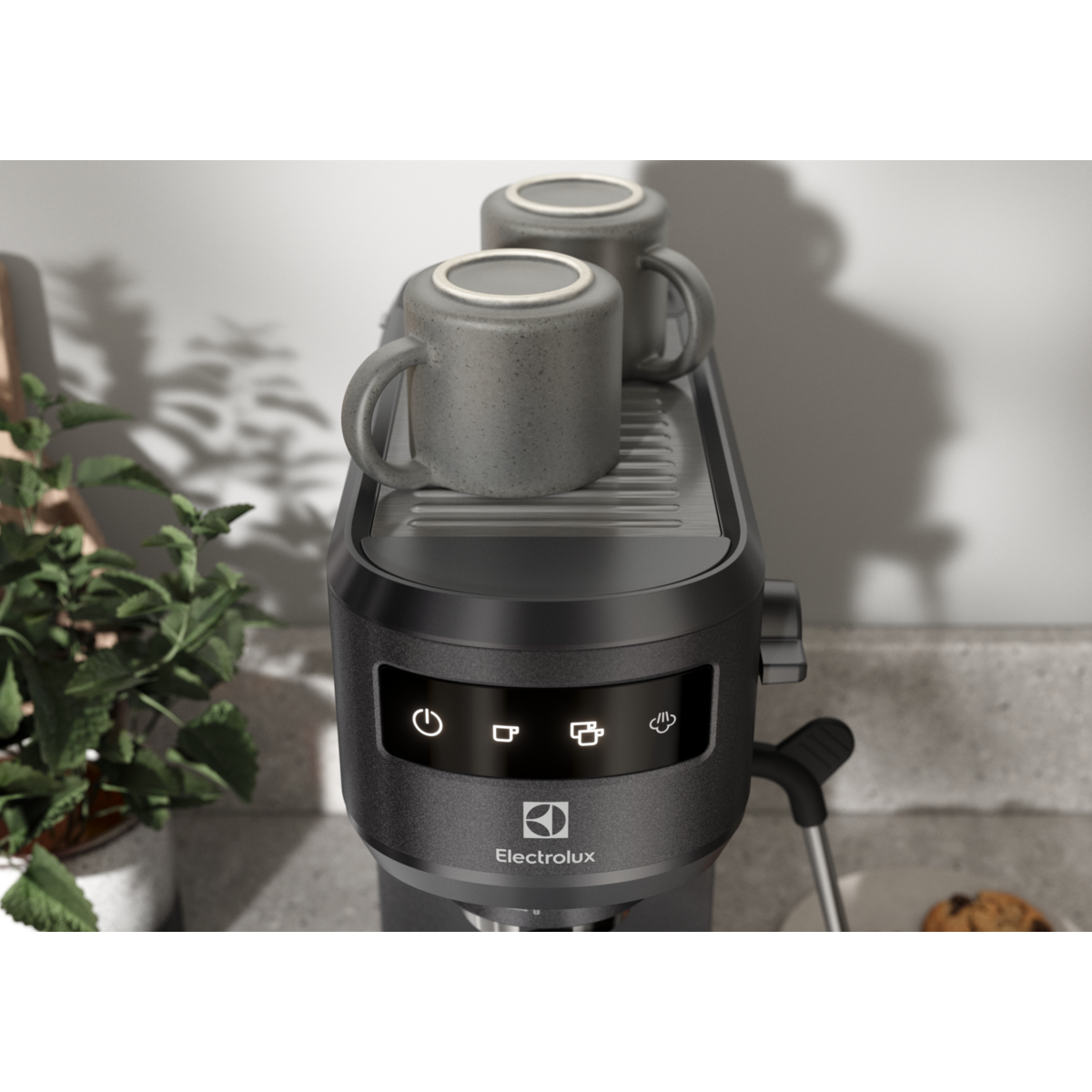 Macchina da caffè nera con due tazze grigie sopra. Il logo Electrolux è visibile sulla parte anteriore.