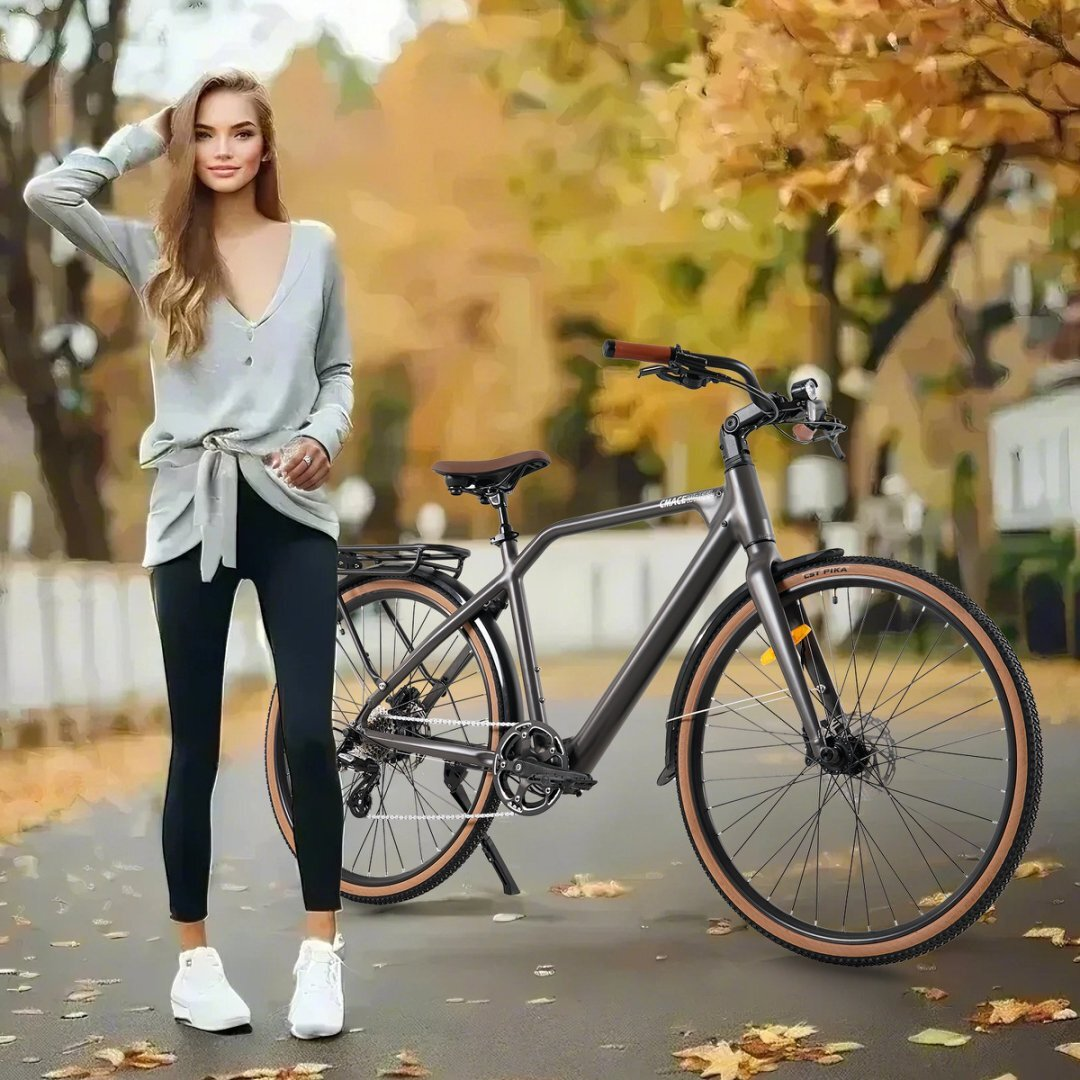 Eine Frau steht neben einem grauen Fahrrad auf einer Straße mit Herbstlaub. Sie trägt einen leichten Pullover.