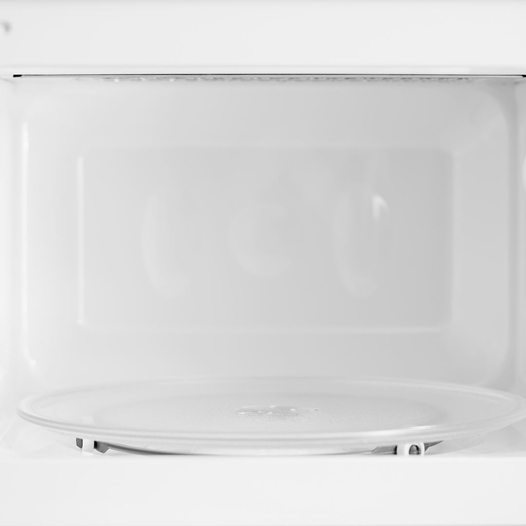 Wnętrze białej kuchenki mikrofalowej z widocznym szklanym talerzem.