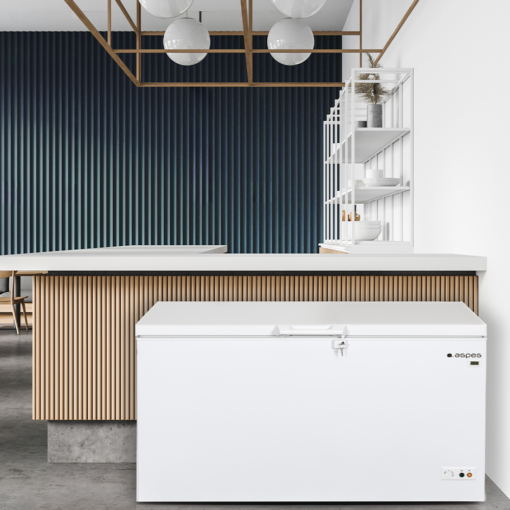 Un congelador horizontal blanco se coloca en una cocina moderna con detalles en blanco y madera.