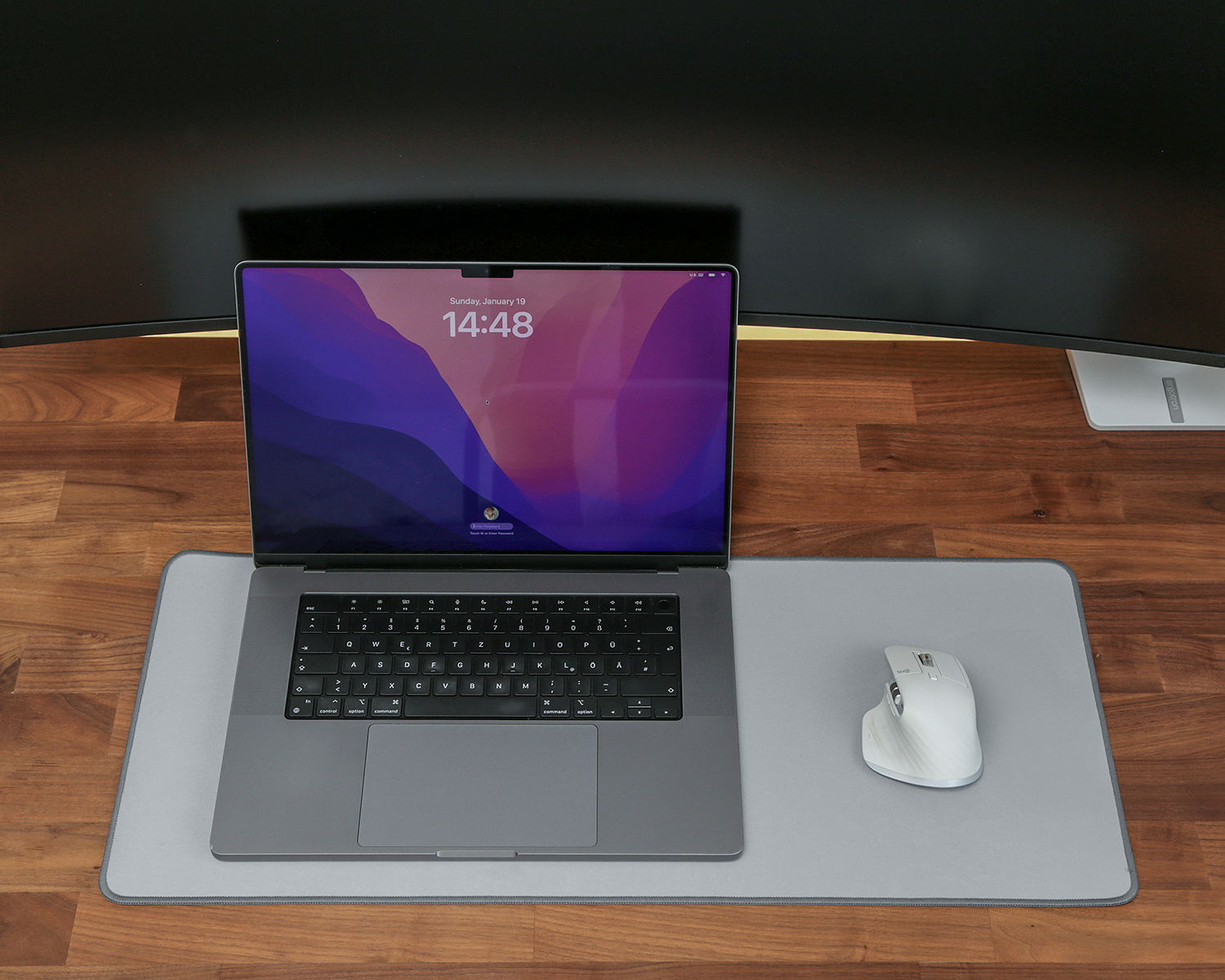 Laptop, Maus auf grauem Mauspad, auf einem Holzschreibtisch. Zwei große Monitore im Hintergrund.