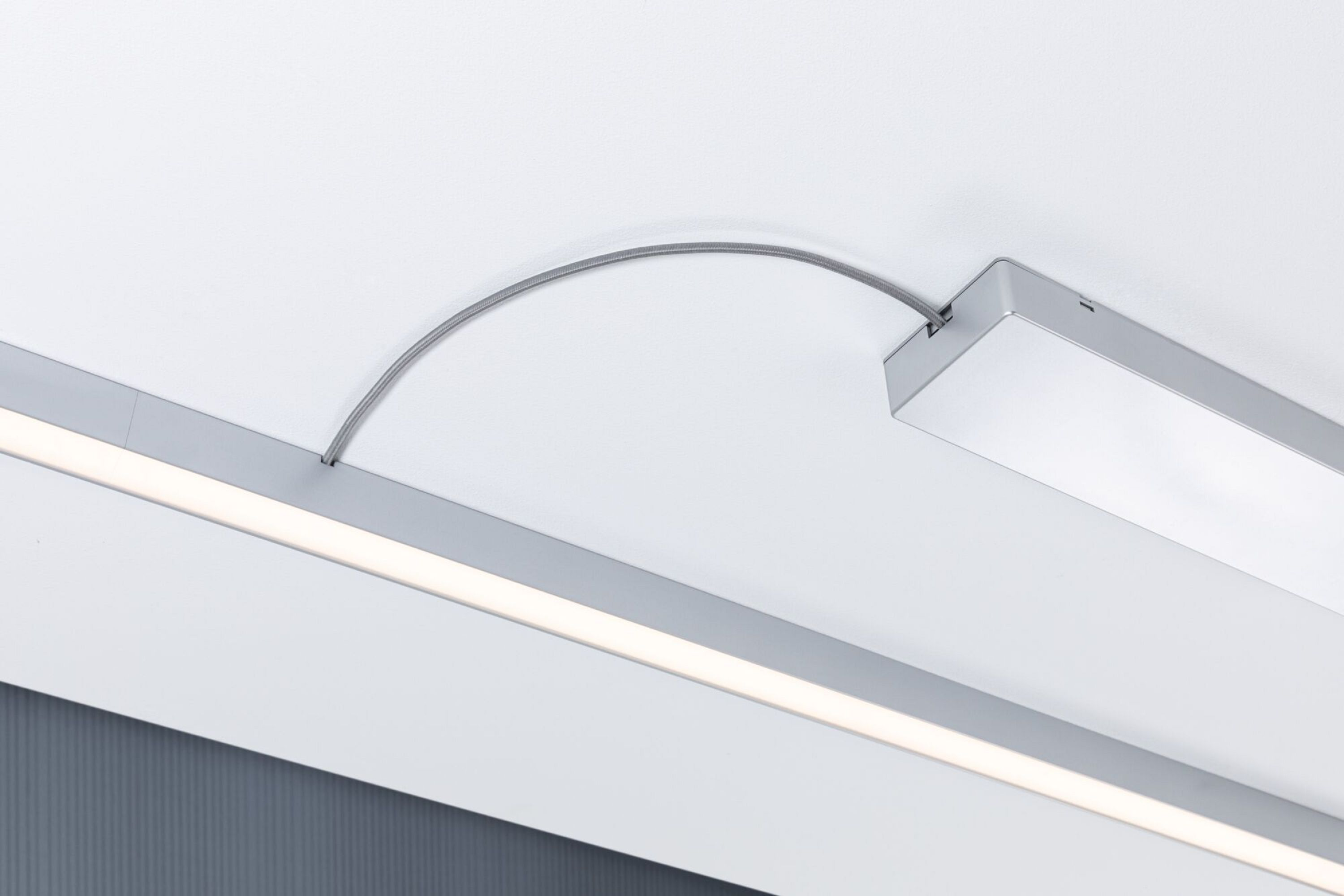 Eine silberne Leuchte an einer weißen Decke, mit einem gebogenen Kabel, das mit der Leuchte verbunden ist.