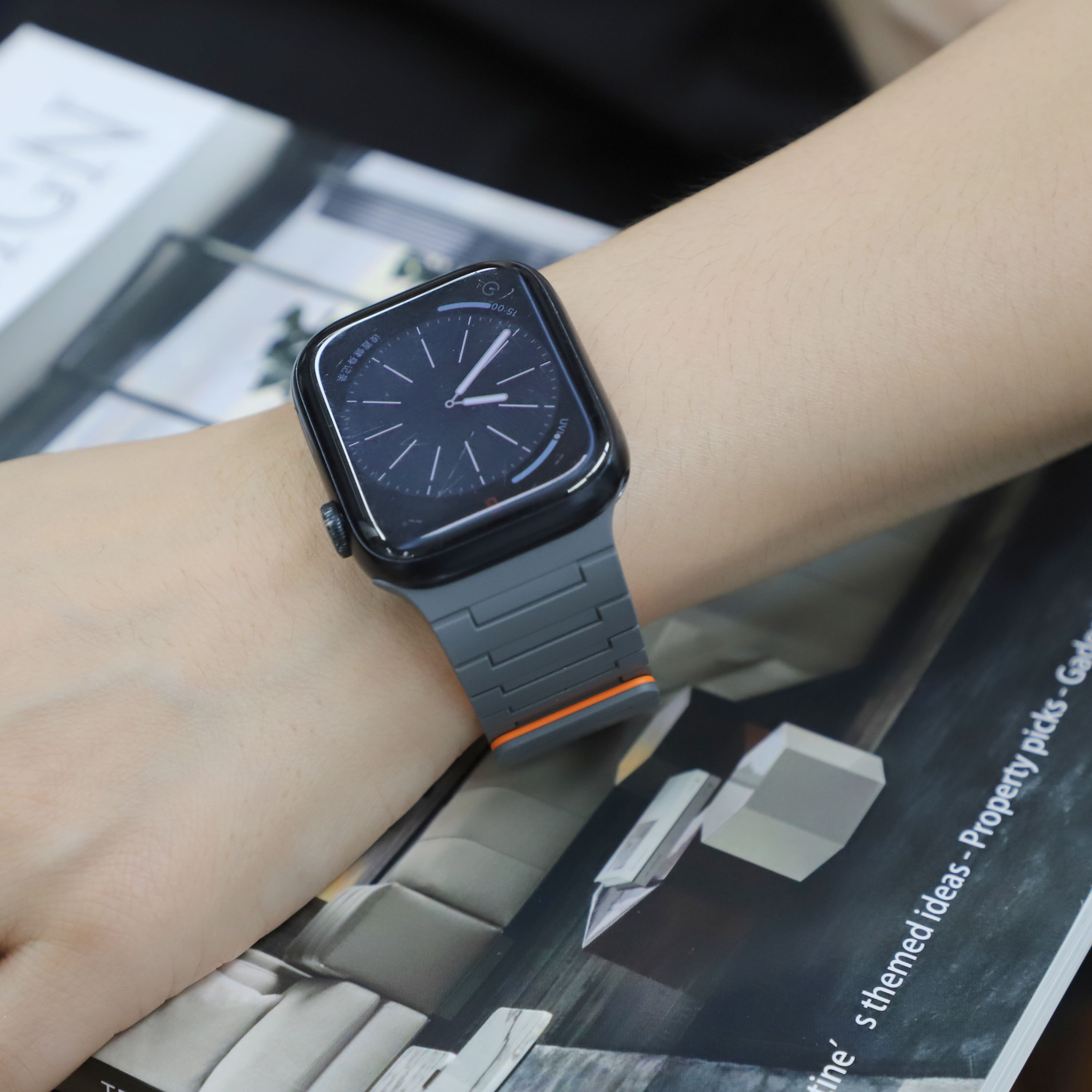 Das Handgelenk einer Person mit Smartwatch, das Band grau, auf einem Magazin.