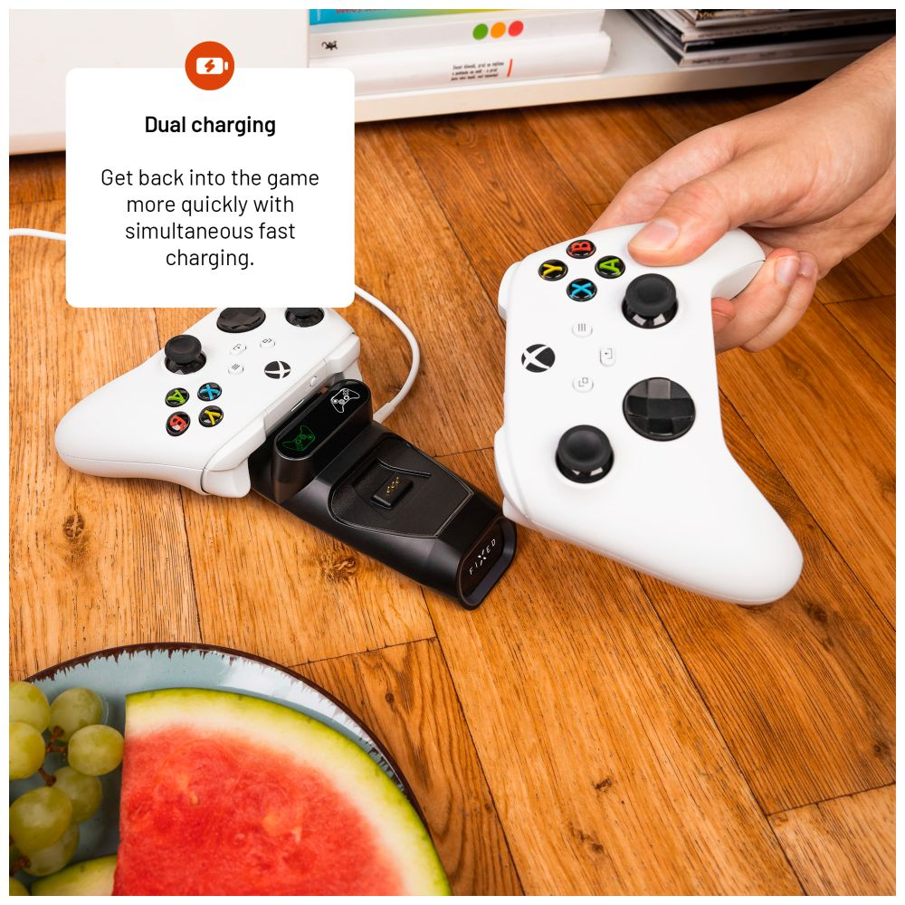 Controller bianchi su una stazione di ricarica, con piatto di frutta e sfondo in legno.
