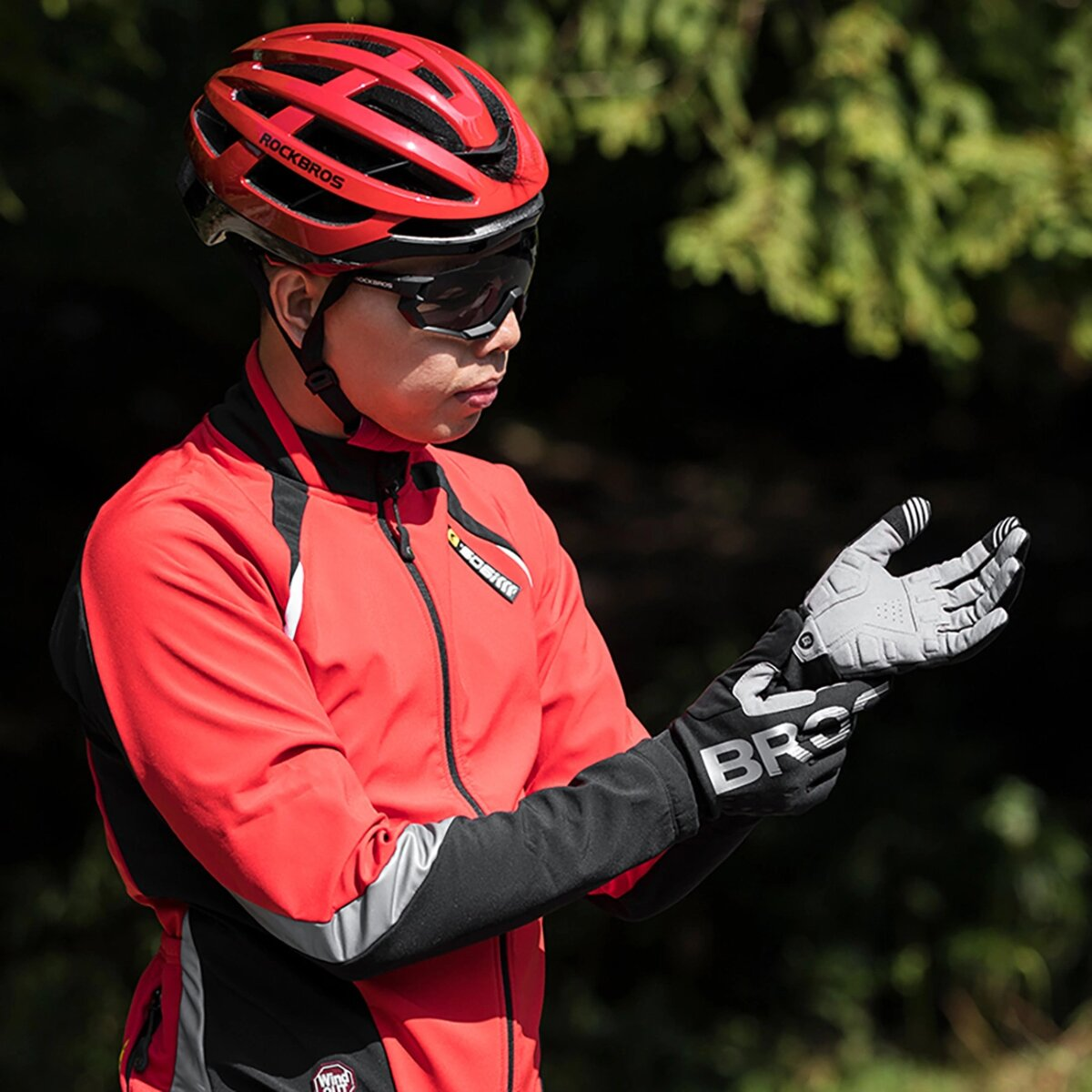 Mann mit rotem Helm, Jacke und Handschuhen, mit verschwommenem grünem Hintergrund.