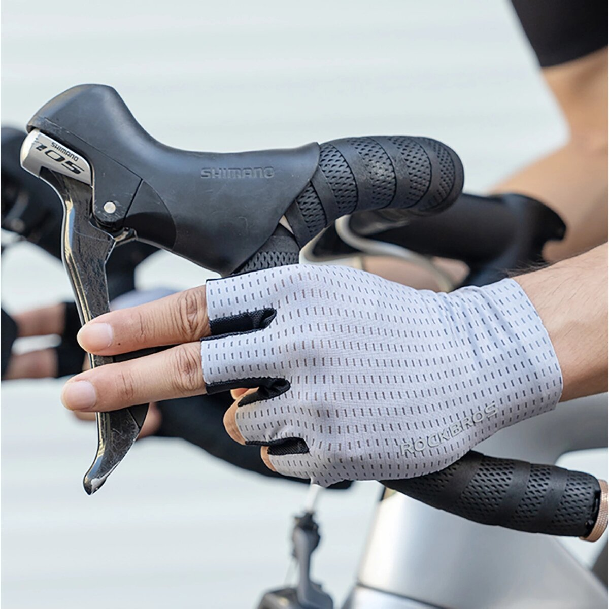 Eine Hand mit einem grauen, fingerlosen Handschuh an der Fahrradbremse. Auf dem Handschuh steht ROCKBROS.