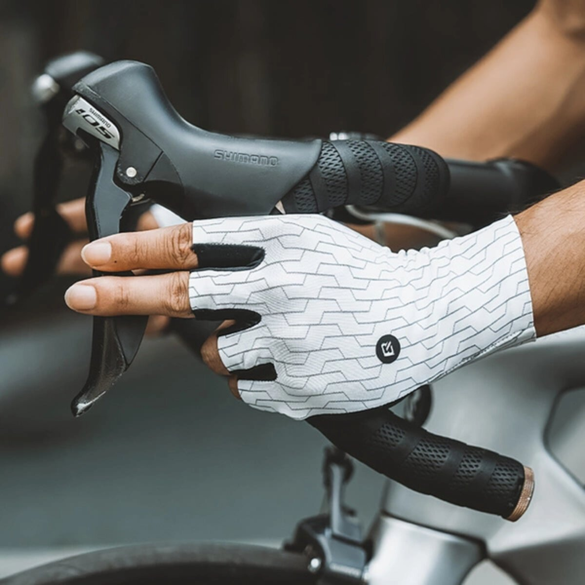Die Hand einer Person an einem Fahrradgriff, die einen weißen Handschuh trägt.