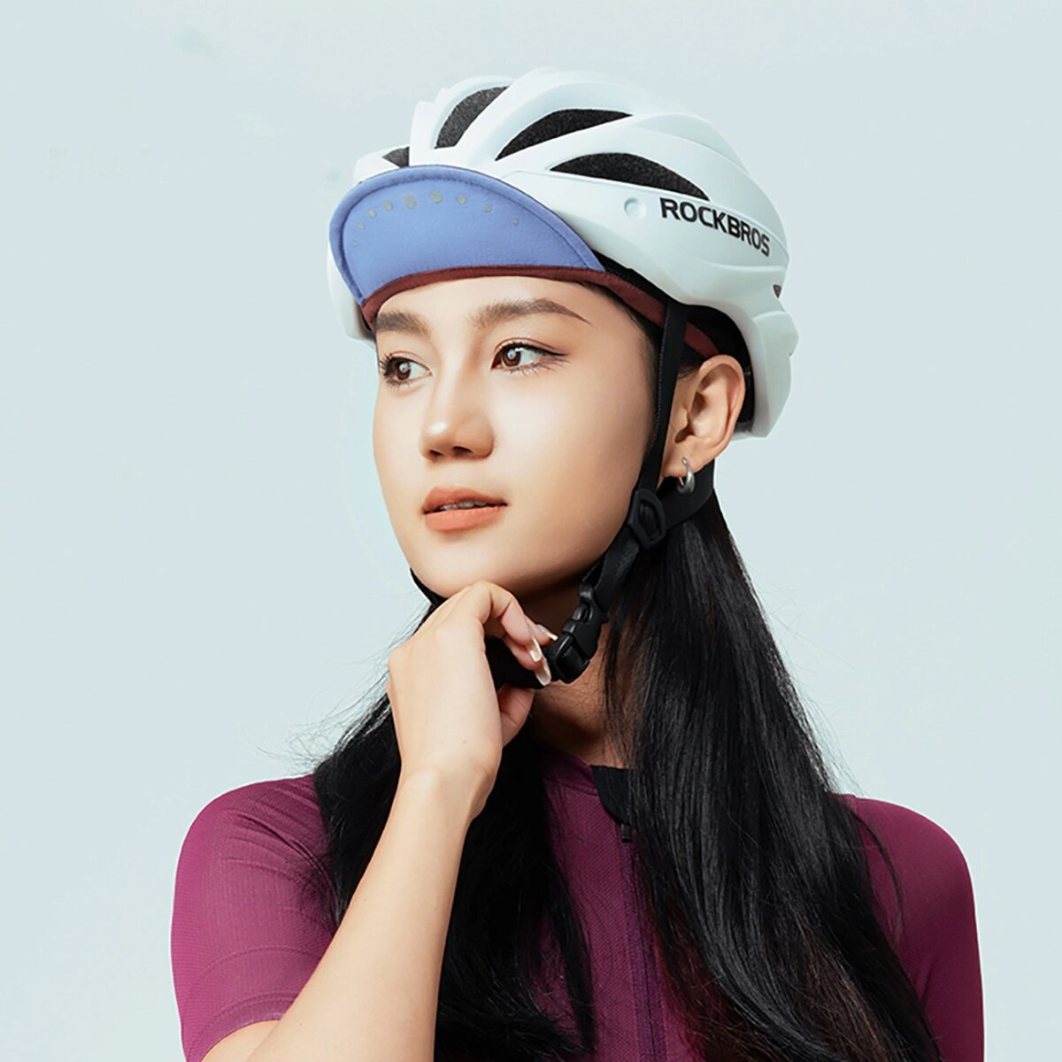 Una donna con un casco da ciclismo con visiera blu, che guarda di lato. Indossa un top bordeaux.