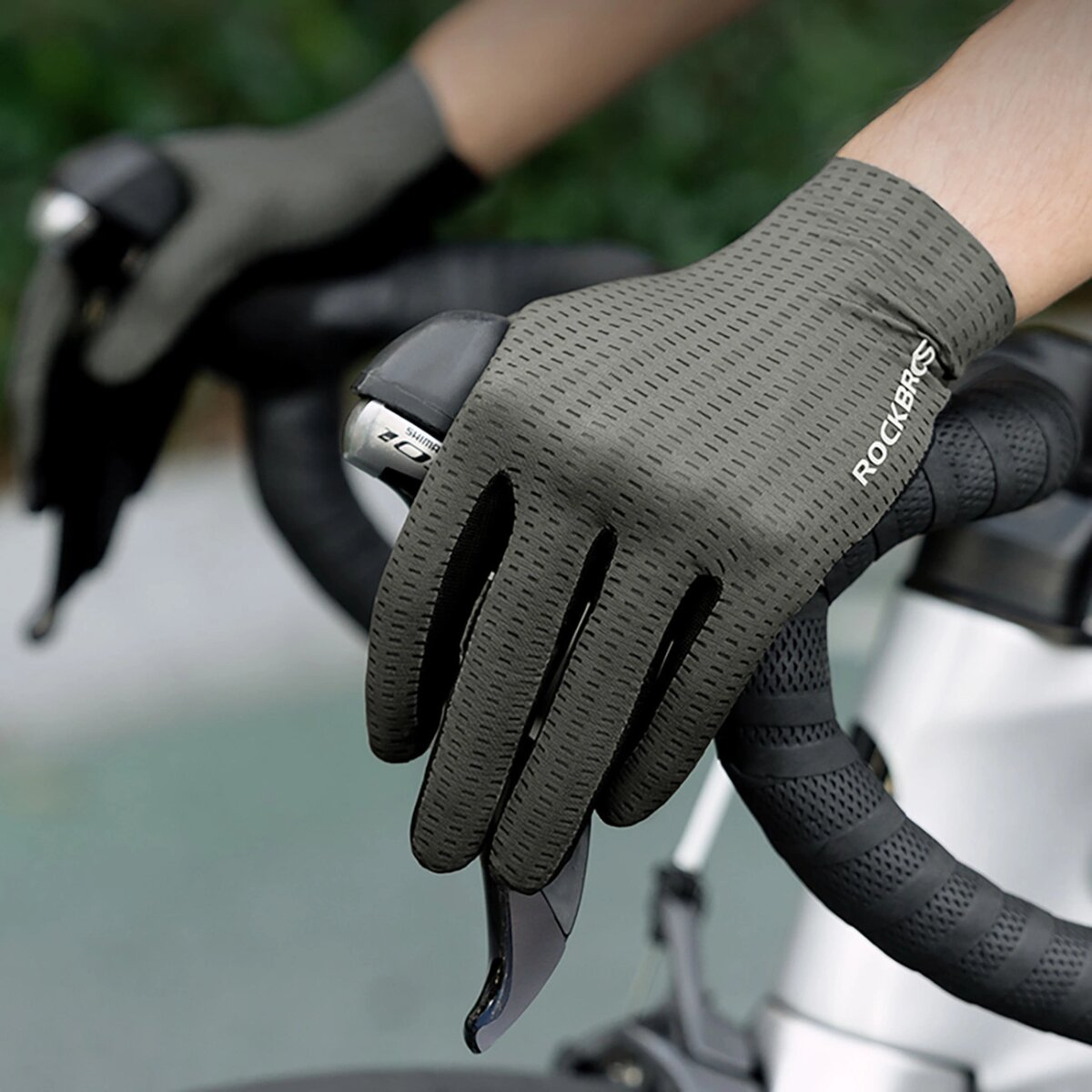 Hände an Fahrradlenkern, mit grauen Rockbros-Handschuhen. Die Ansicht ist aus der Perspektive des Fahrers.