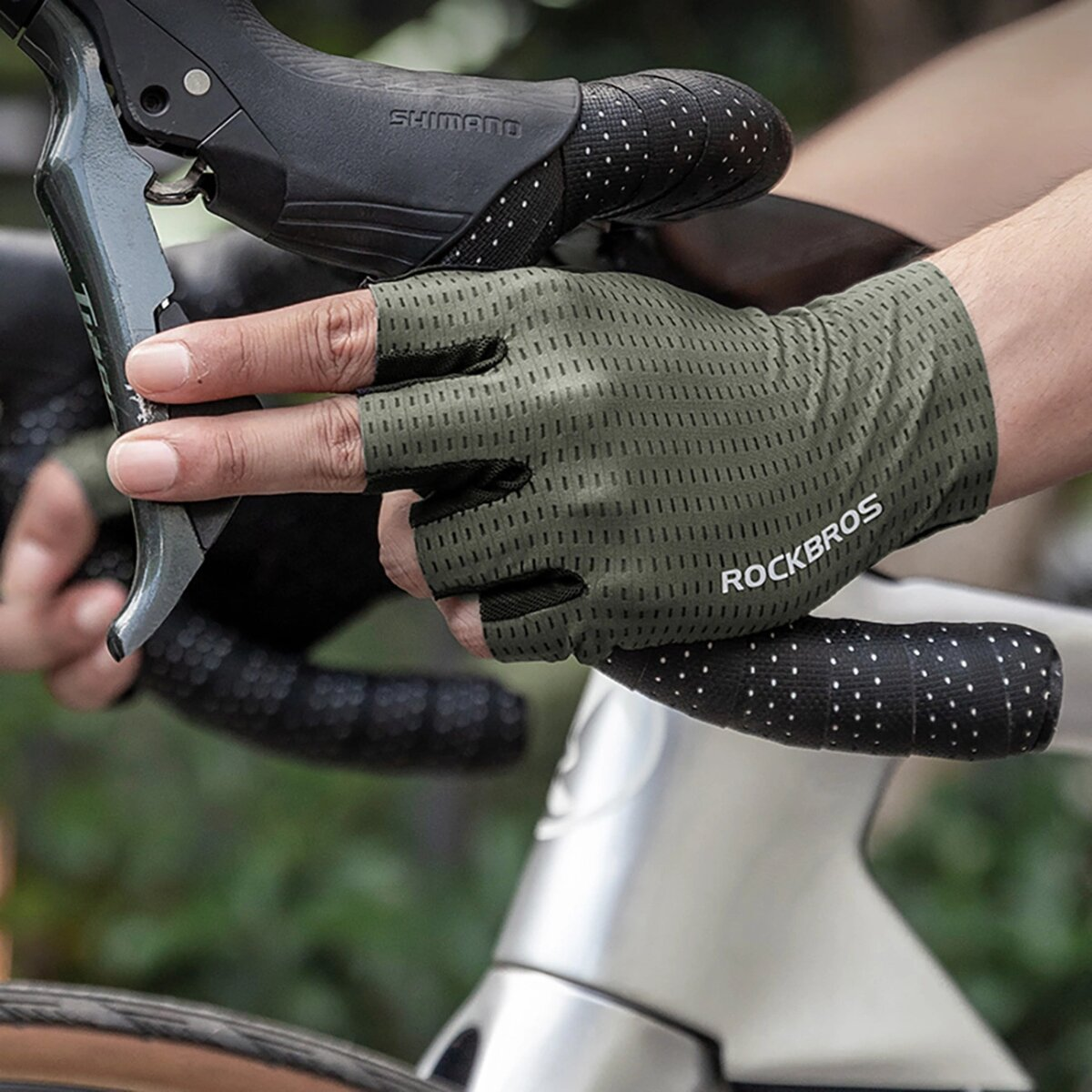 Hände mit grünen Radhandschuhen an einem Fahrradlenker, SHIMANO sichtbar. Schwarzes, gepunktetes Lenkerband.