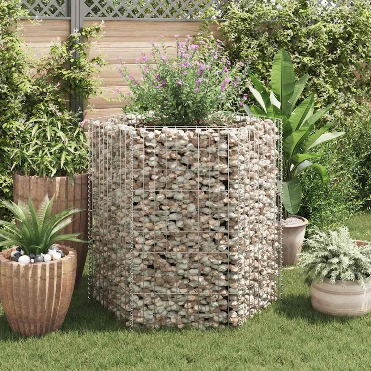 Eine Gartenszene mit einem Gabionenpflanzer, gefüllt mit Steinen und Pflanzen im Hintergrund.