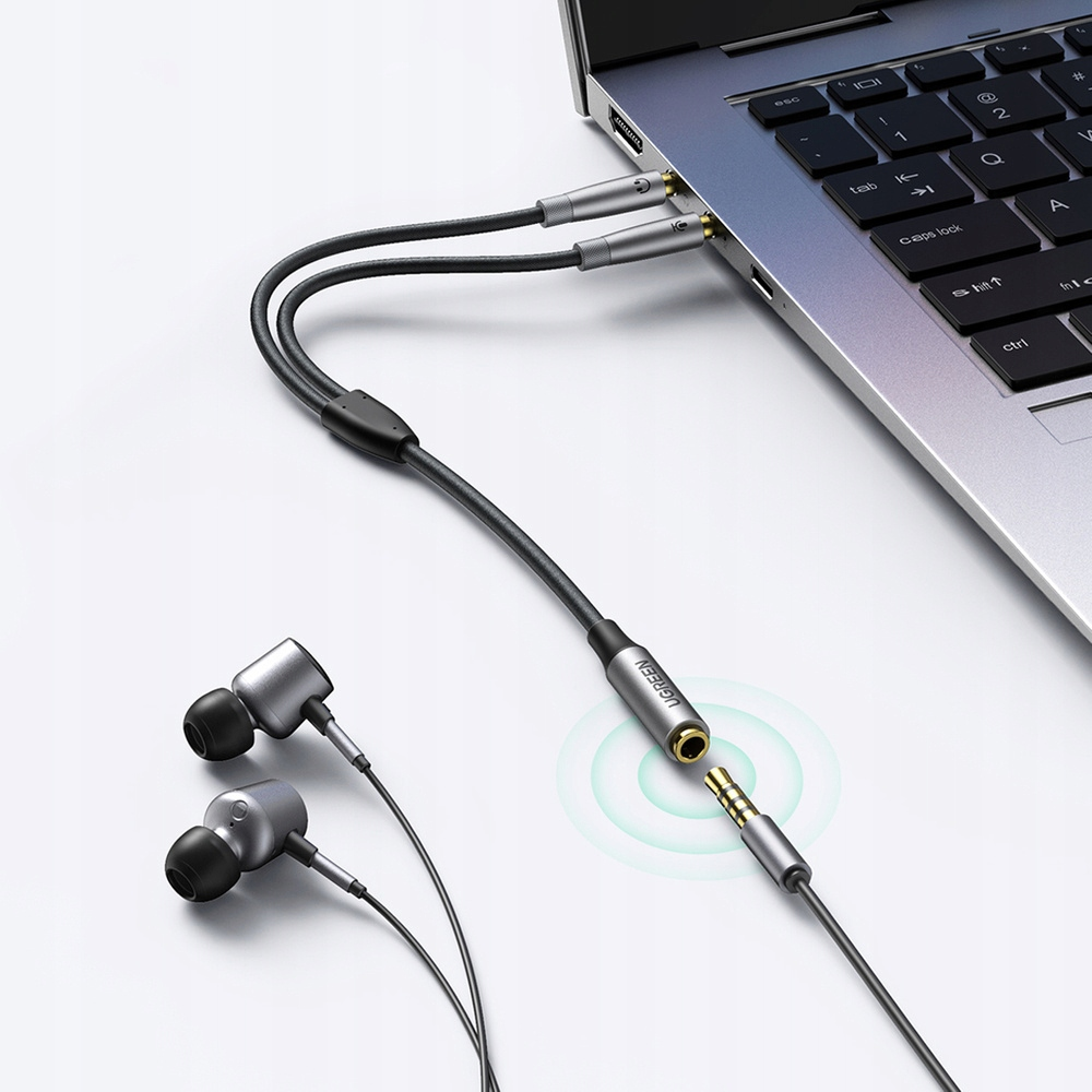 Un primo piano di un laptop collegato a auricolari tramite uno splitter. Lo splitter è argentato.