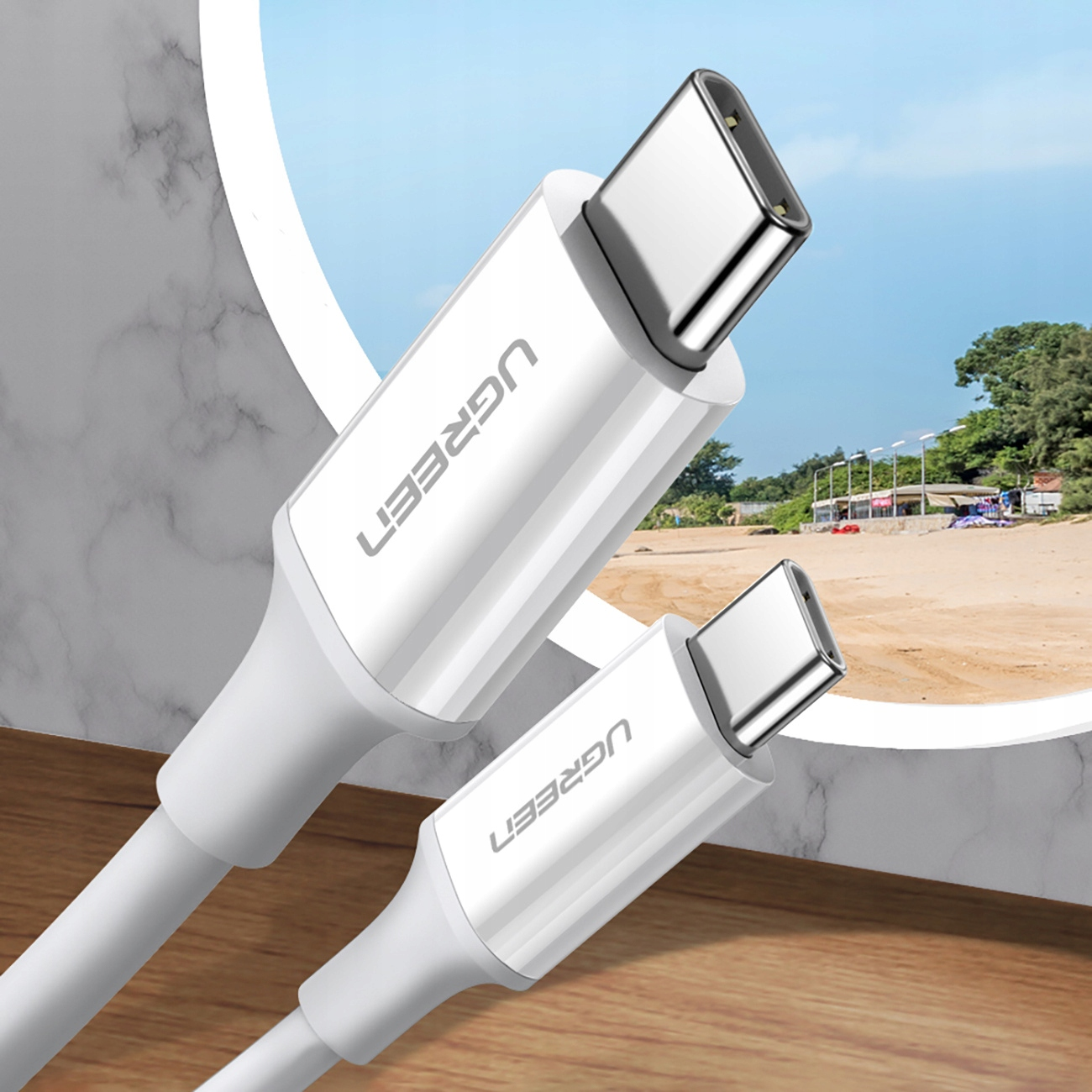 Dwa białe kable USB-C z marką UGREEN. Tłem jest scena plażowa z błękitnym niebem.