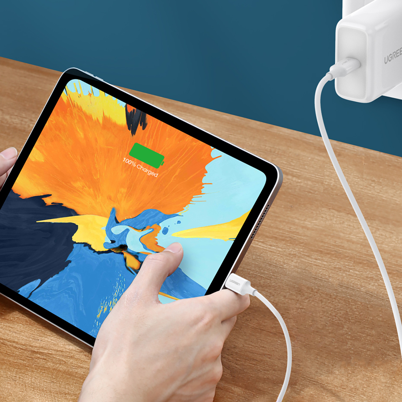 iPad jest ładowany białą ładowarką i kablem. Ekran pokazuje ikonę naładowania 100%.