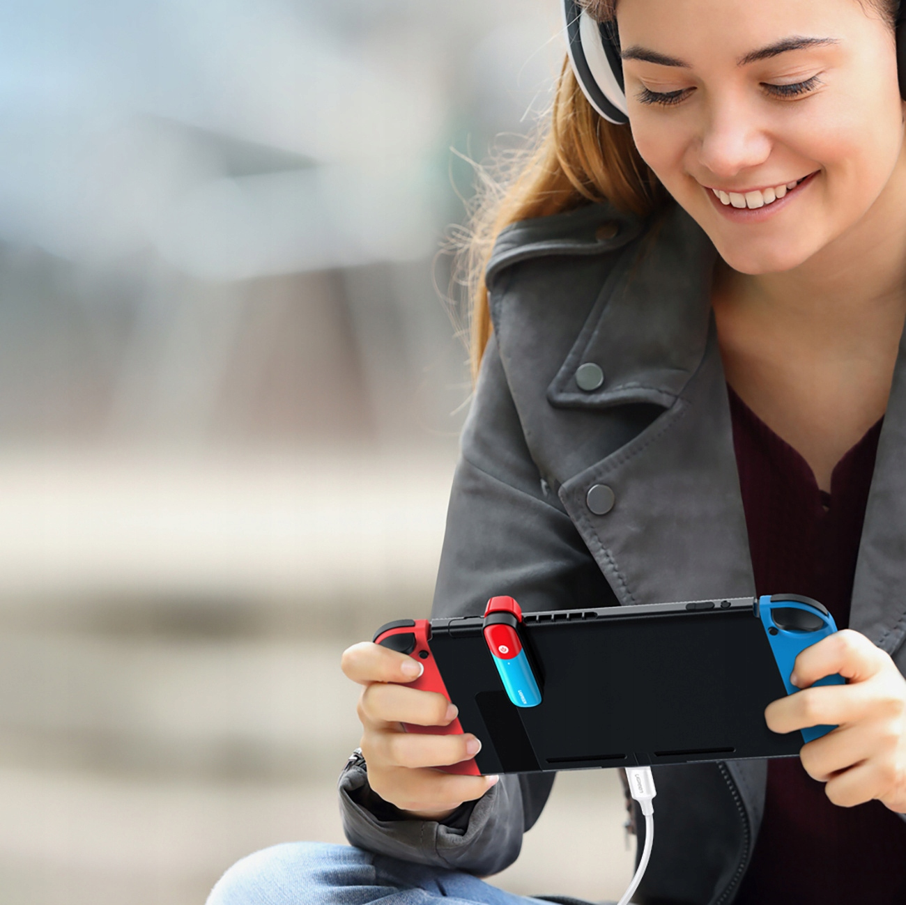 Kobieta w słuchawkach uśmiecha się, trzymając czarny kontroler do gier. Tło jest rozmyte.