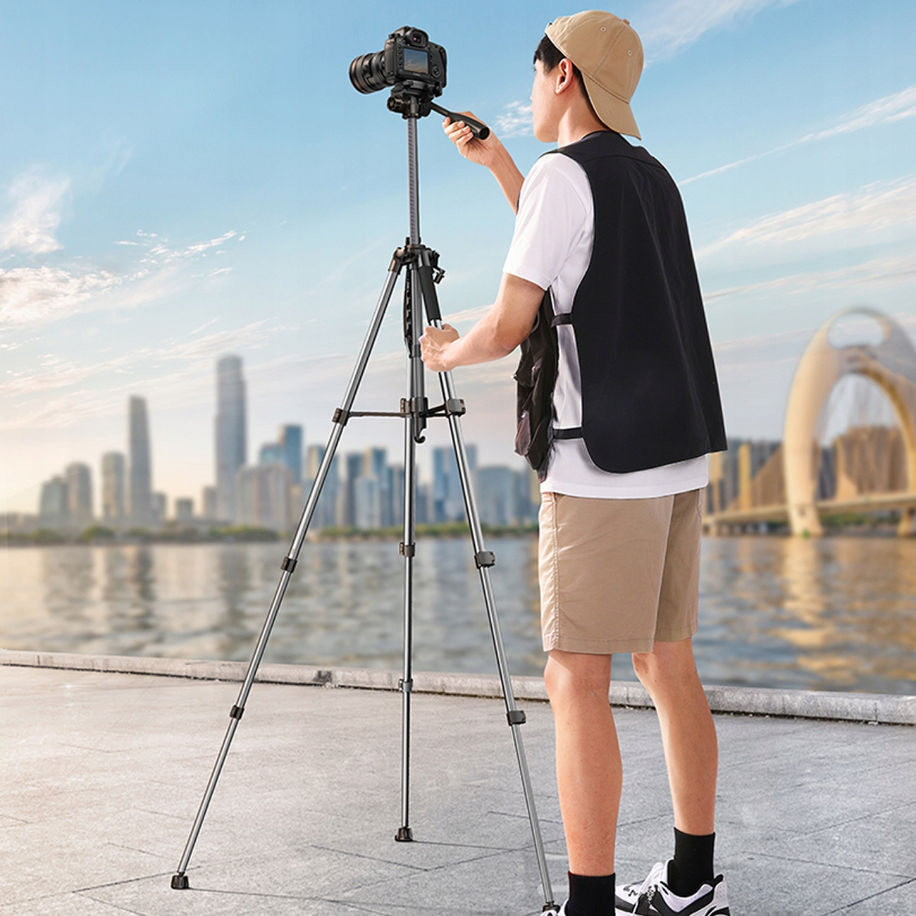 Bir kişi, bir şehir ve gökyüzünün önünde bir tripod üzerine bir kamera kuruyor.