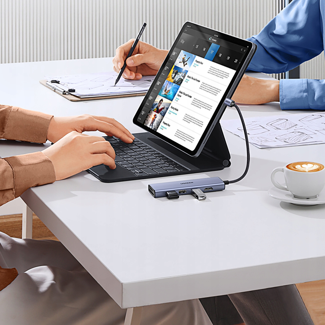 Osoba używa tabletu z klawiaturą. Podłączony jest hub UGREEN, a na stole filiżanka kawy.