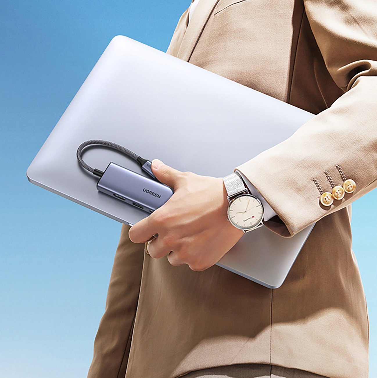 Osoba trzyma srebrny laptop z podłączonym hubem UGREEN. Osoba ma na sobie zegarek ze srebrną bransoletą.