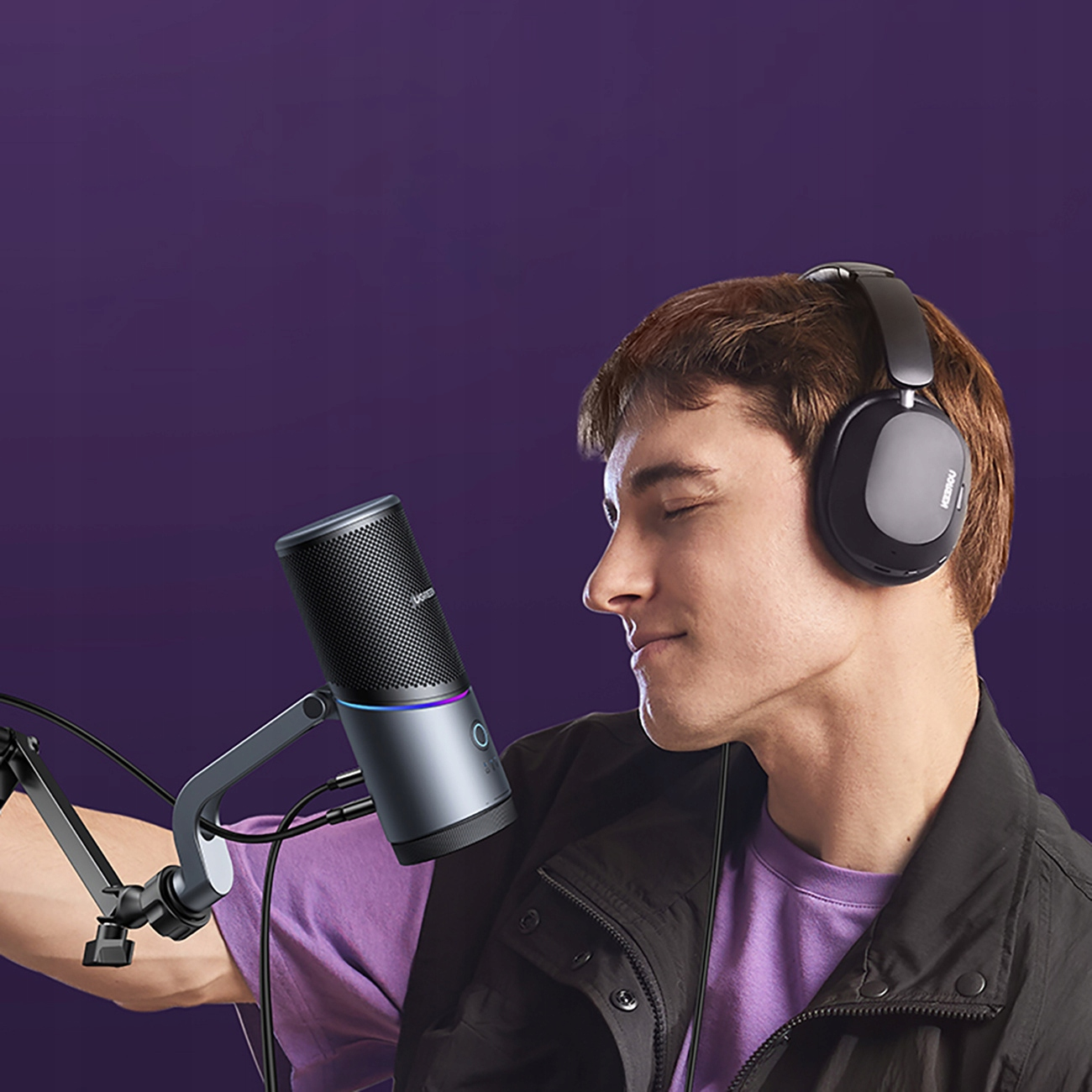 Mężczyzna w słuchawkach mówi do mikrofonu przymocowanego do wysięgnika. Fioletowe tło.