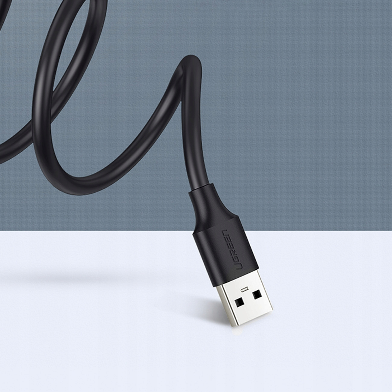 Czarny kabel USB UGREEN ze złączem USB-A. Tło jest turkusowe i szare.