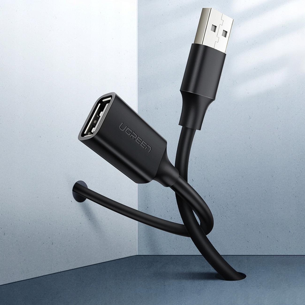 Kabel adaptera USB firmy UGREEN jest pokazany na tle jasnoniebieskiej ściany.