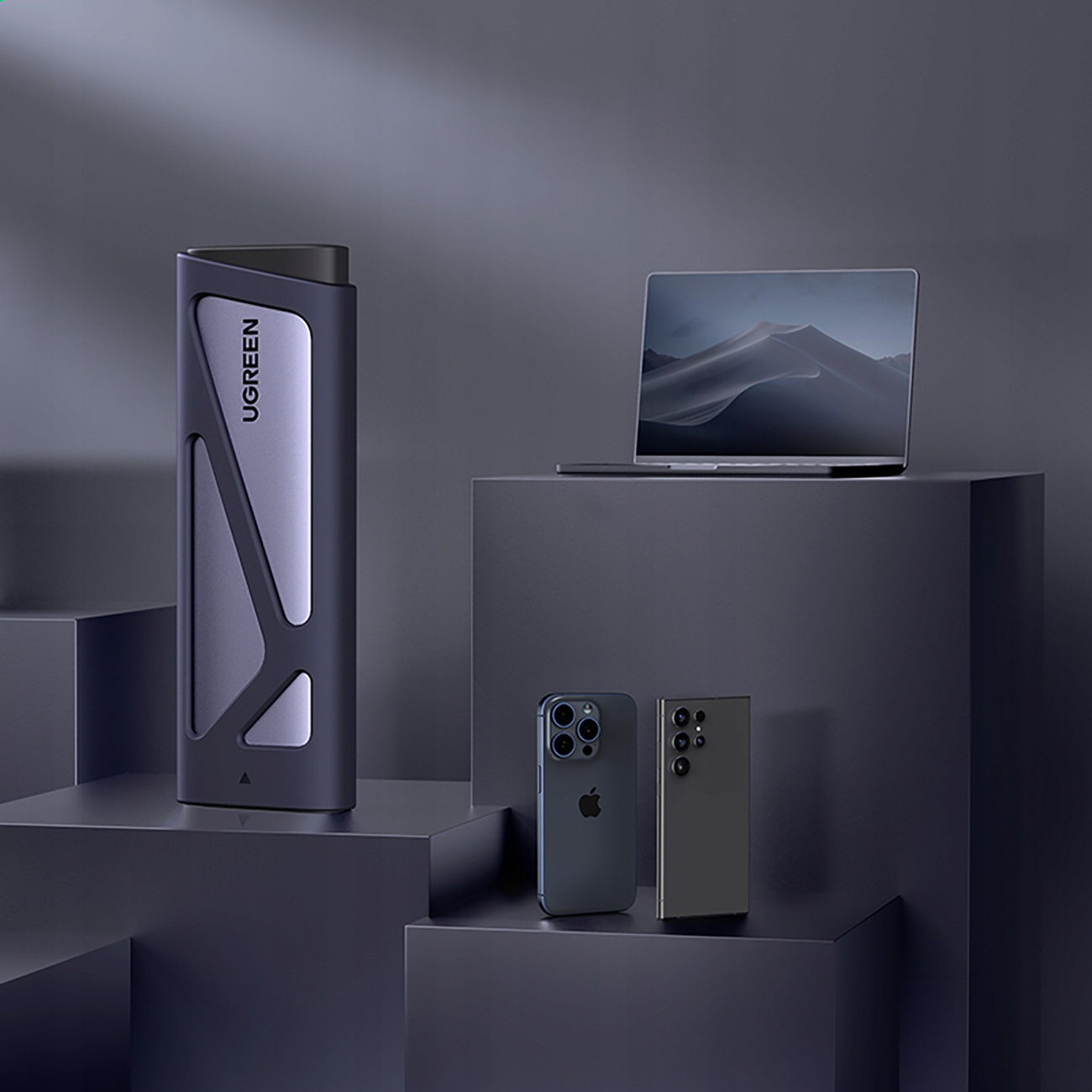 Zewnętrzny dysk SSD UGREEN, iPhone i laptop na szarych blokach na ciemnoszarym tle.