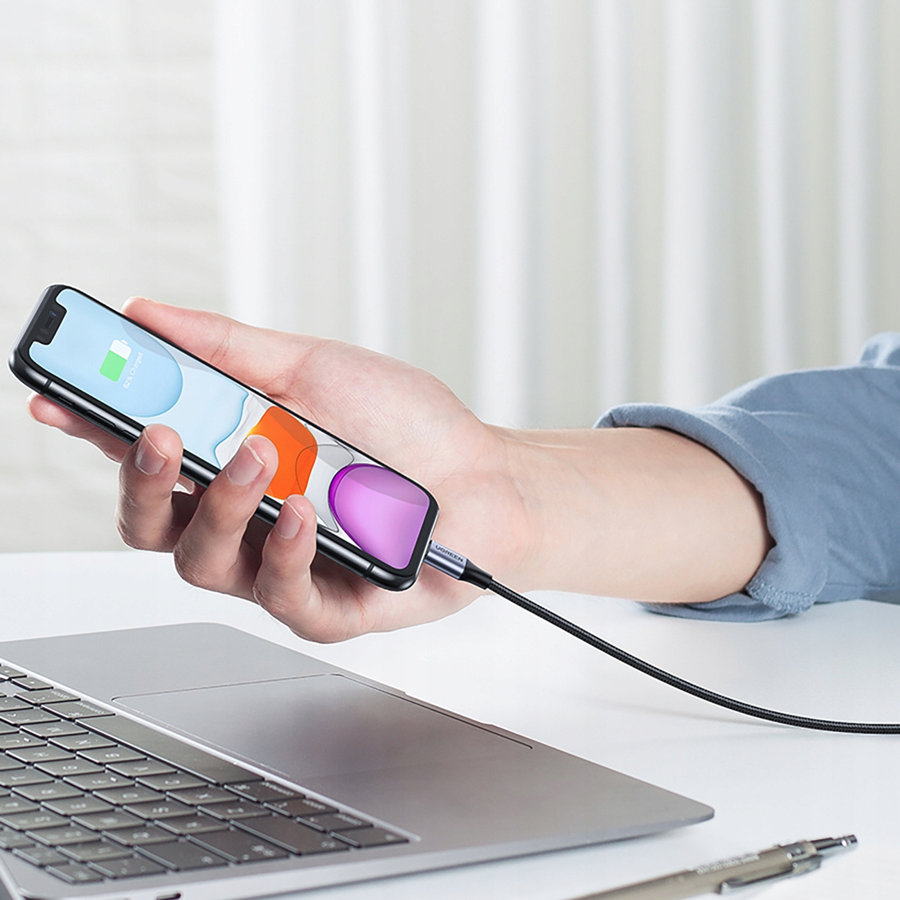 Bir kişi, bir akıllı telefon tutuyor ve bir UGREEN kablosuyla bir dizüstü bilgisayara bağlı. Telefon pil şarjını gösteriyor.