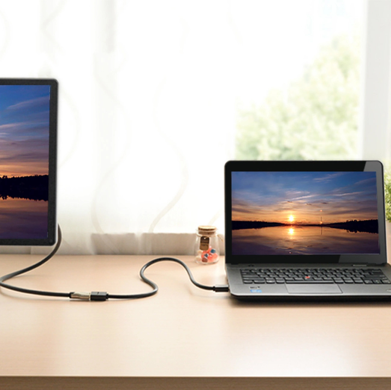 Laptop i monitor zewnętrzny połączone kablem. Obraz zachodu słońca na obu ekranach.