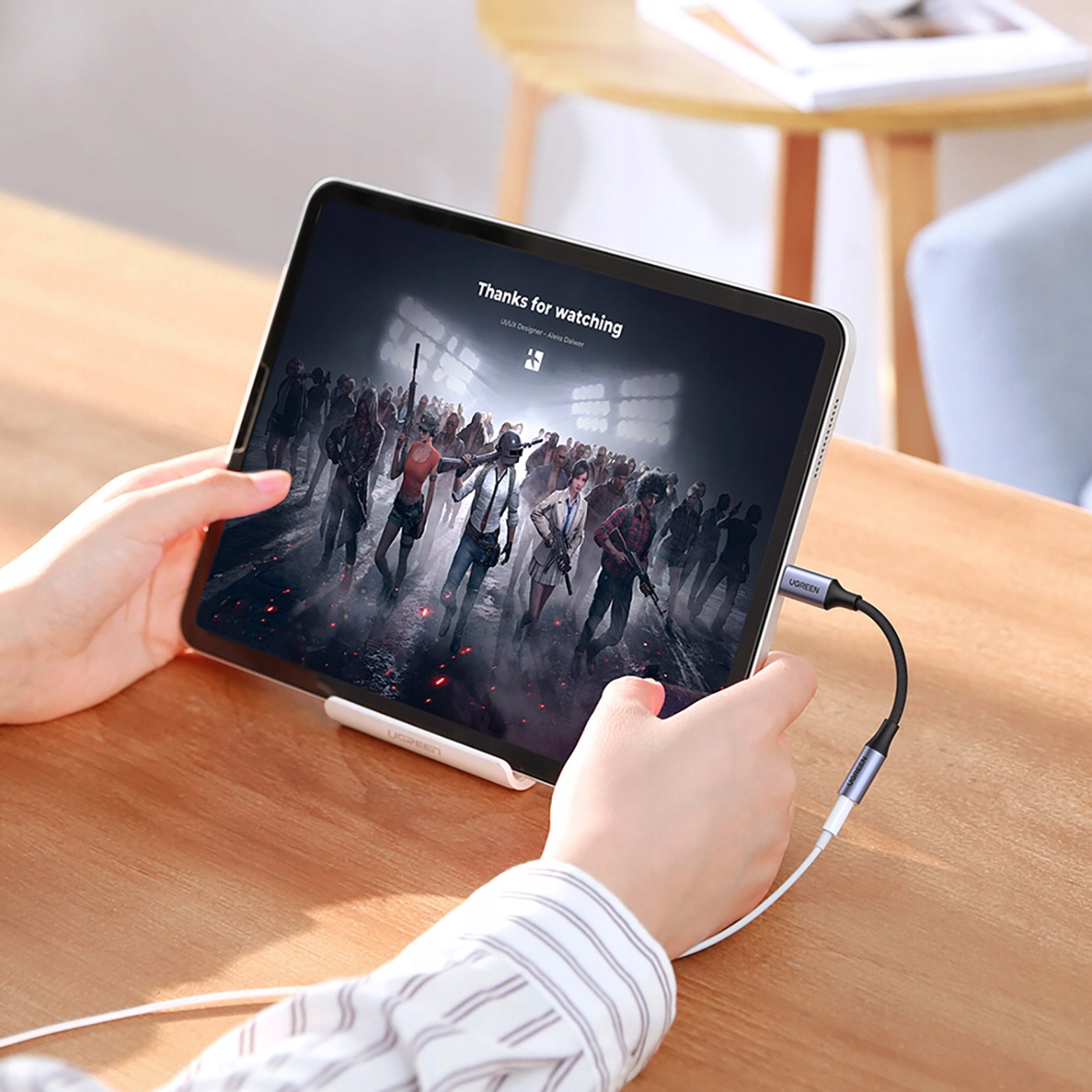 Tablet podłączony do adaptera audio UGREEN białym kablem na drewnianym stole.