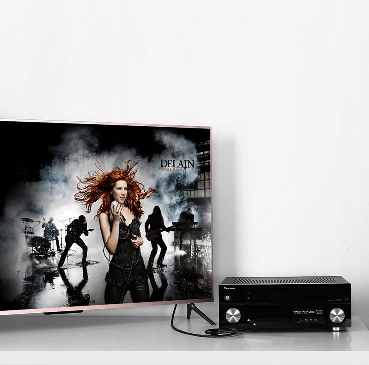 Ekran telewizora z występem zespołu i systemem nagłośnieniowym na białej powierzchni.