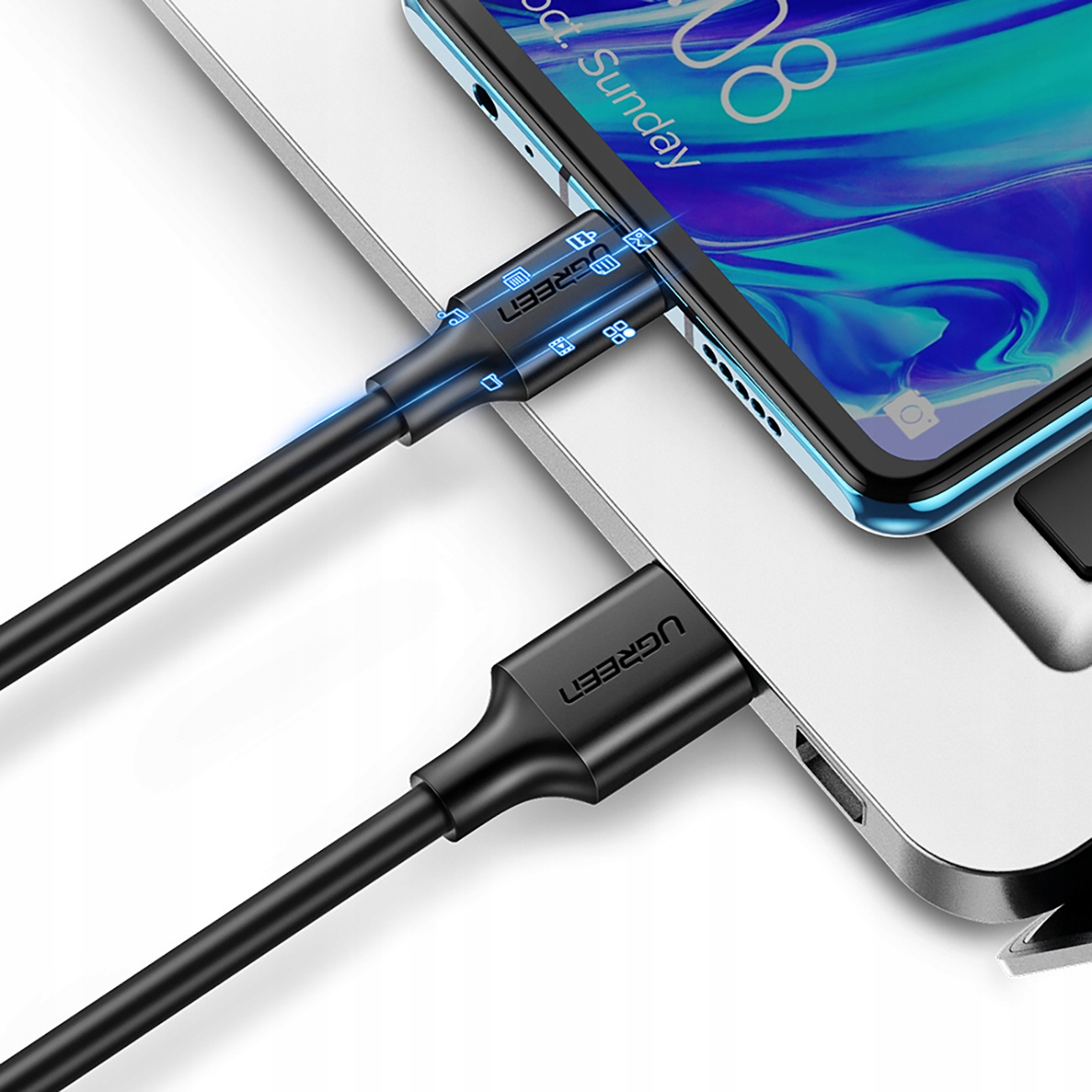 Zbliżenie na telefon w trakcie ładowania. Czarny kabel ładujący jest podłączony do telefonu i laptopa.