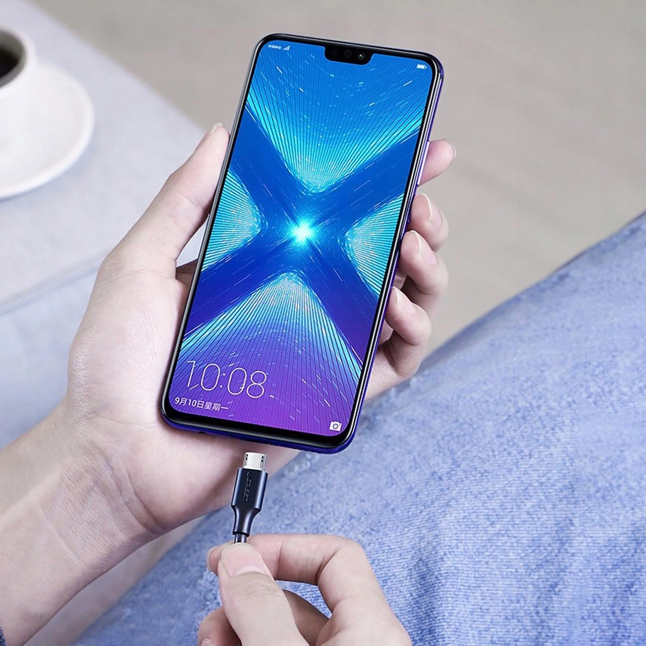 Osoba trzymająca telefon z podłączonym kablem USB-C. Telefon wyświetla niebieskie i fioletowe tło.