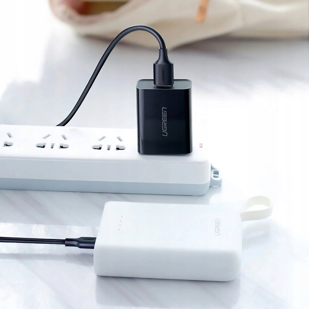 Czarna ładowarka podłączona do listwy zasilającej. Biały power bank jest podłączony do ładowarki kablem.