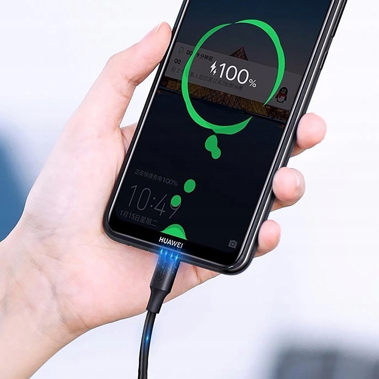 Ręka trzyma telefon ładujący się kablem UGREEN. Ekran pokazuje 100% naładowania.