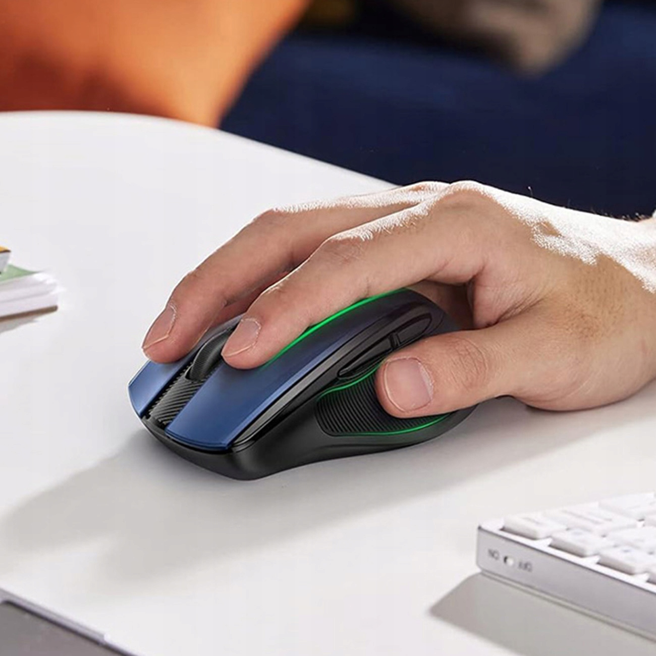 Ręka używająca niebiesko-czarnej myszy bezprzewodowej na białej powierzchni. Świeci zielone światło.