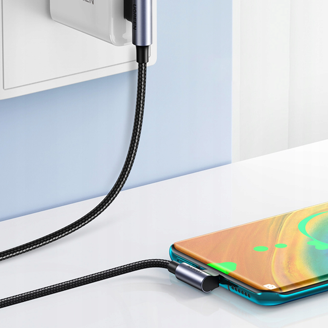 Czarny kabel UGREEN ładujący telefon. Telefon jest podłączony. Gniazdo ścienne w tle.
