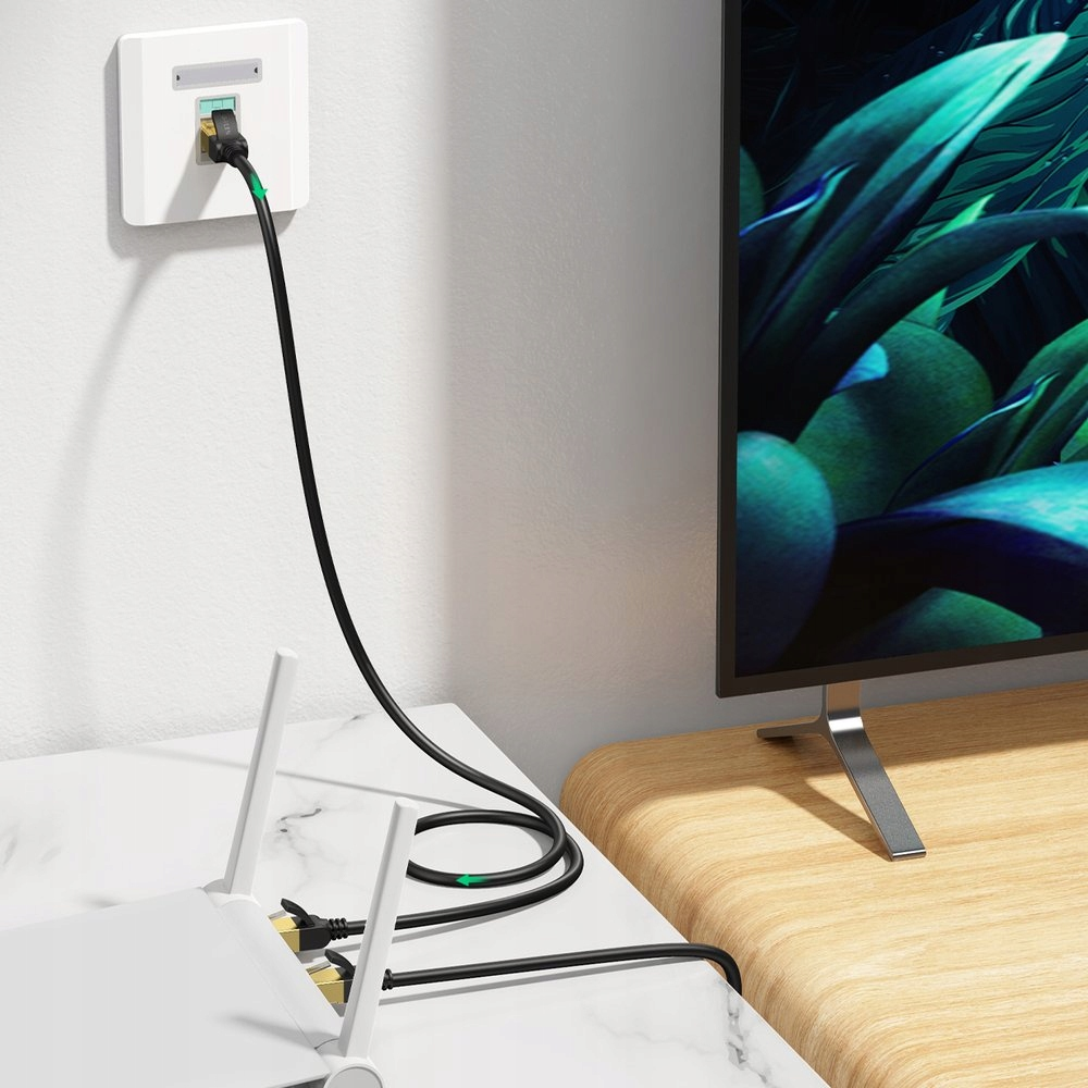 Czarny kabel Ethernet podłączony do gniazdka ściennego, routera i telewizora. Biała ściana i drewniany stół.