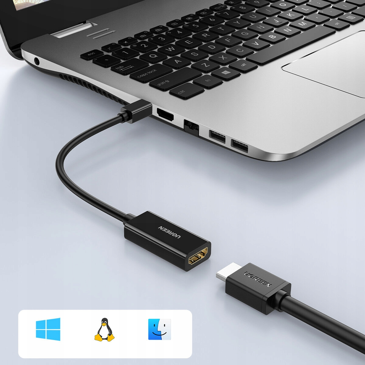 Laptop podłączony do monitora za pomocą czarnego kabla. Laptop wyświetla ikony Windows, Linux i Mac.