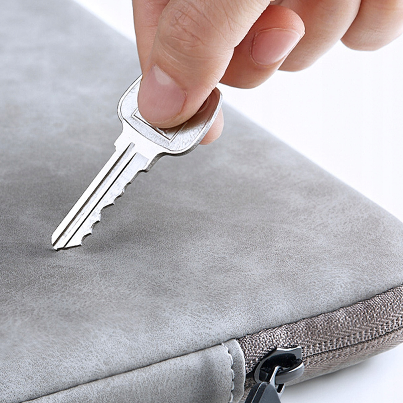 Ręka trzymająca klucz w pobliżu szarej obudowy. Obudowa ma zamek błyskawiczny i teksturowaną powierzchnię. Klucz jest blisko zamka błyskawicznego.
