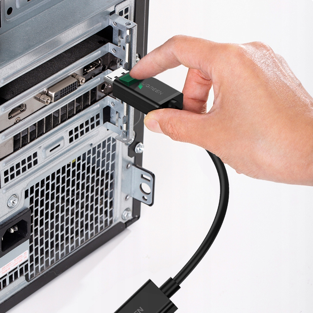 Ręka podłączająca adapter UGREEN do komputera. Adapter jest czarny, a komputer z tyłu.