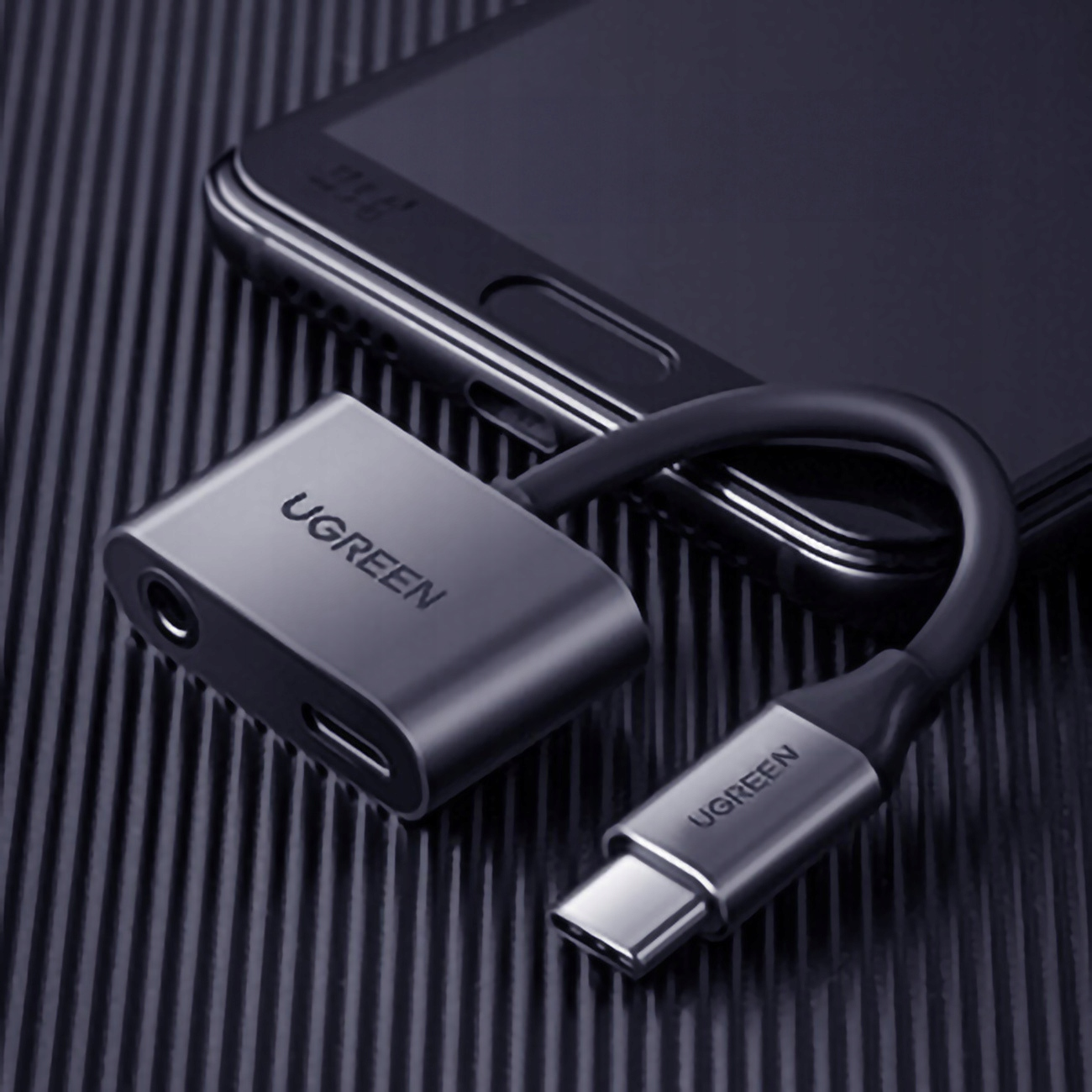 Czarny adapter UGREEN z gniazdem słuchawkowym i portem USB-C podłączonym do telefonu.