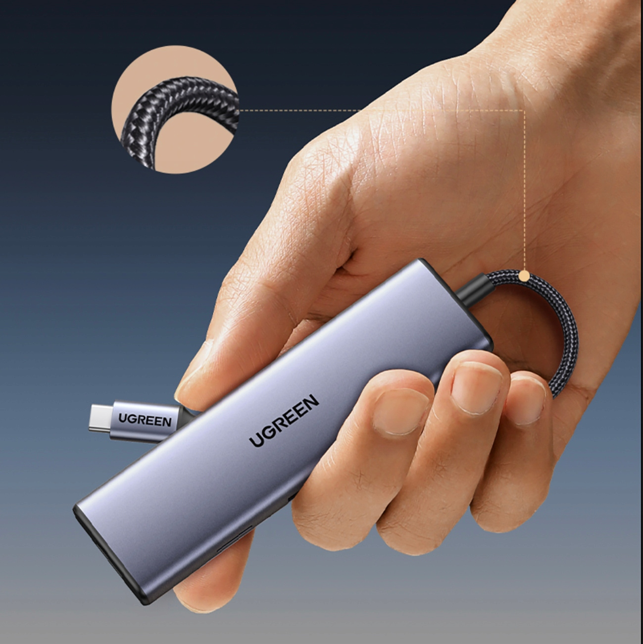 Dłoń trzymająca hub UGREEN. Urządzenie jest szare z nazwą marki. Dołączony jest pleciony kabel.