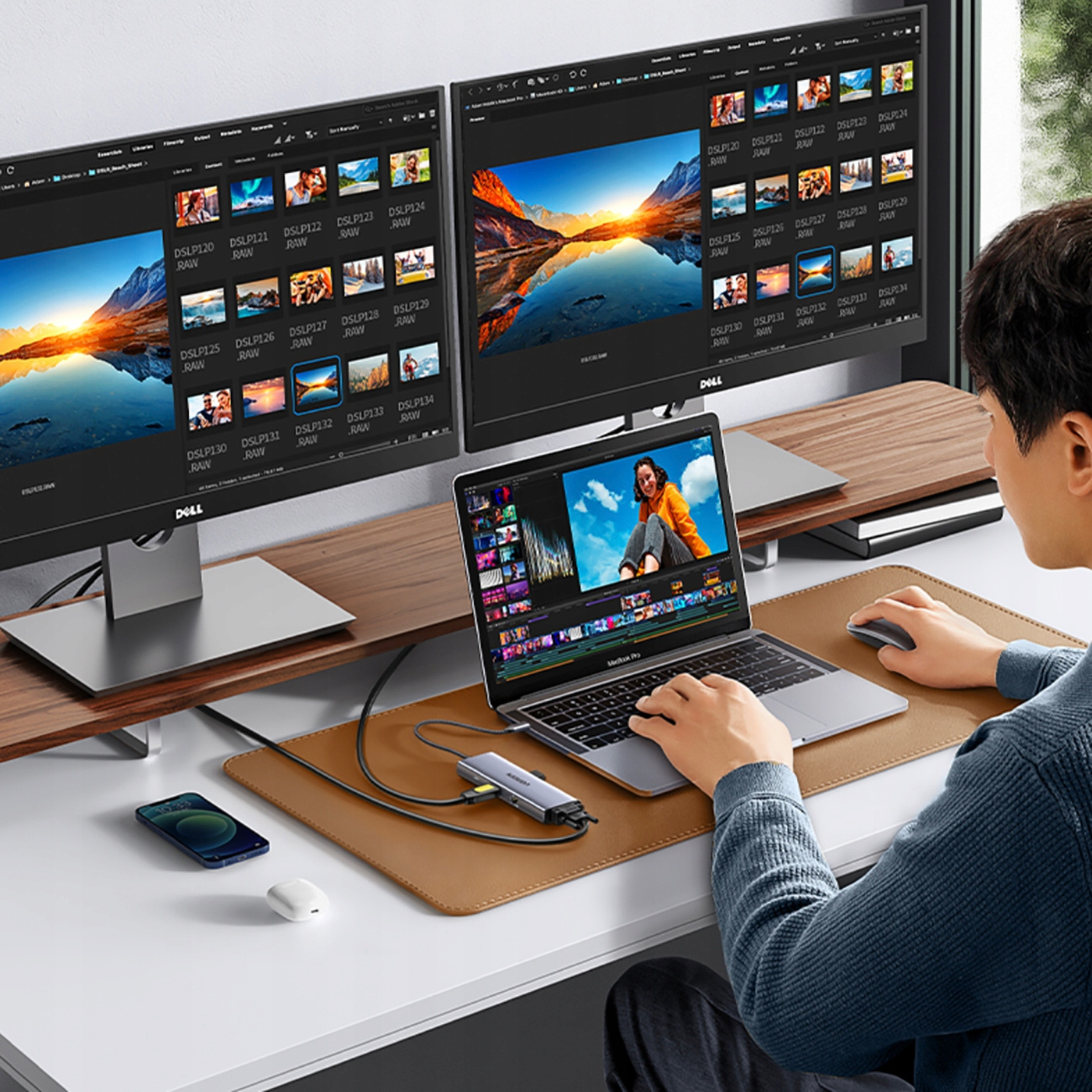 Mężczyzna edytuje wideo na laptopie podłączonym do dwóch monitorów. Obecny jest telefon i mysz.