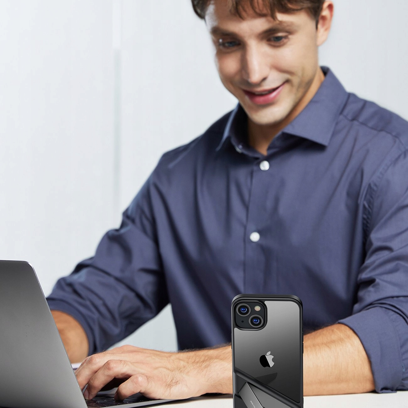 Un uomo sta lavorando su un laptop e tiene un telefono. Il telefono è in una custodia con il logo Apple.